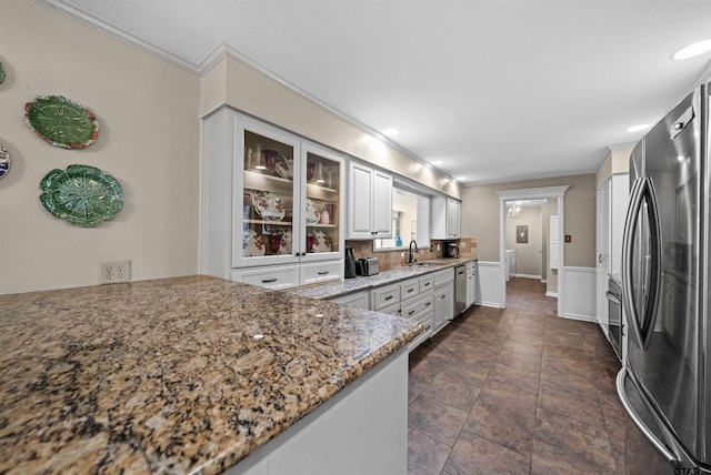 kitchen with stainless steel appliances, white cabinets, sink, ornamental molding, and light stone countertops