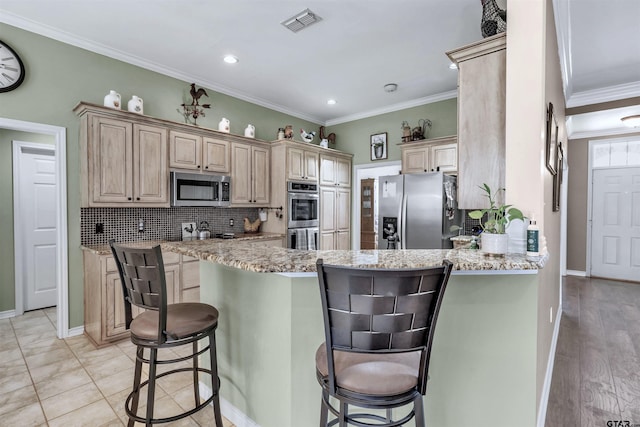 kitchen with kitchen peninsula, appliances with stainless steel finishes, light stone counters, crown molding, and a breakfast bar area