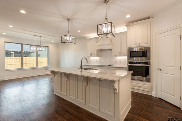 kitchen with an island with sink, appliances with stainless steel finishes, pendant lighting, and light stone counters