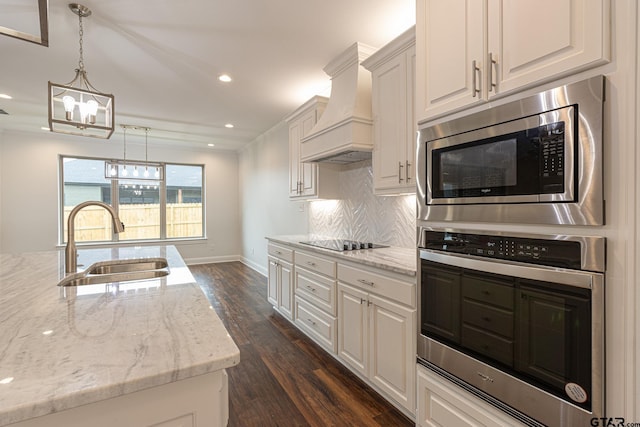 kitchen with sink, premium range hood, stainless steel appliances, white cabinets, and decorative light fixtures