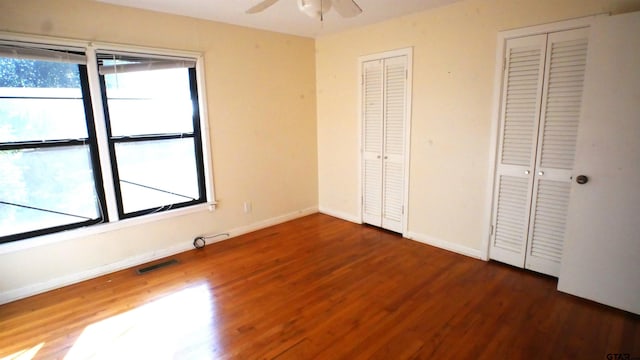 unfurnished bedroom with ceiling fan, dark hardwood / wood-style flooring, multiple windows, and two closets