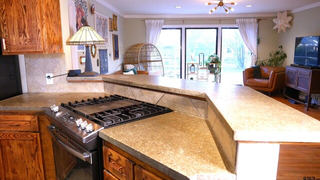 kitchen with a chandelier, stainless steel gas stove, tasteful backsplash, and ornamental molding