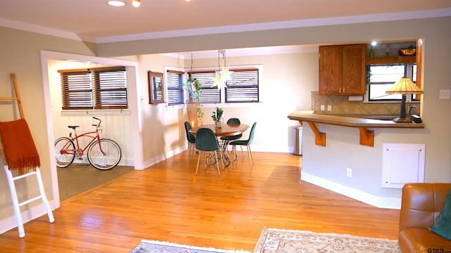 kitchen with a kitchen bar, backsplash, sink, light hardwood / wood-style flooring, and hanging light fixtures