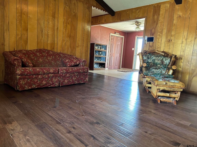 living area with dark hardwood / wood-style flooring, wooden walls, beamed ceiling, and ceiling fan