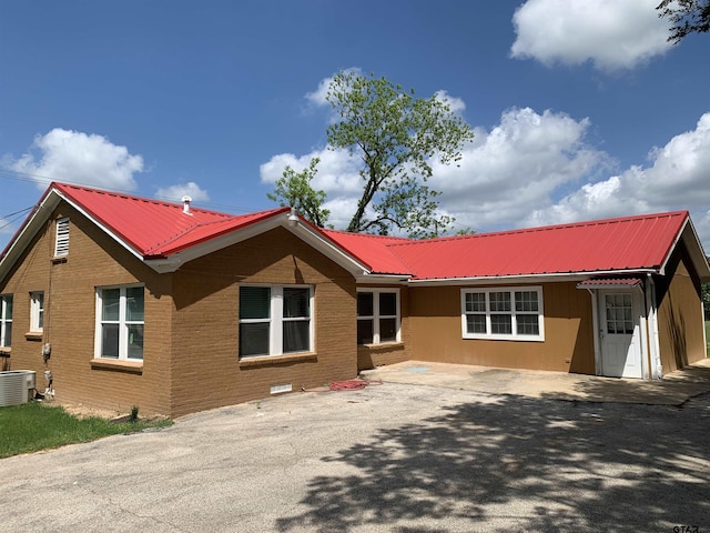 view of front of home featuring metal roof, central AC unit, and brick siding