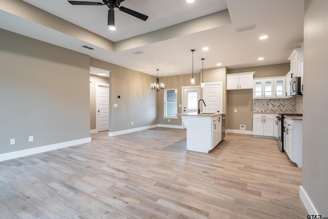 kitchen with sink, white cabinetry, stainless steel appliances, a center island with sink, and a raised ceiling