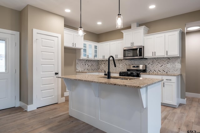 kitchen with stainless steel appliances, white cabinetry, hanging light fixtures, and a center island with sink