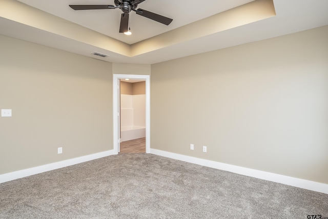 carpeted spare room with a raised ceiling and ceiling fan