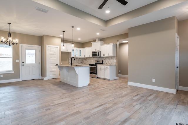 kitchen featuring appliances with stainless steel finishes, tasteful backsplash, white cabinetry, hanging light fixtures, and a center island with sink