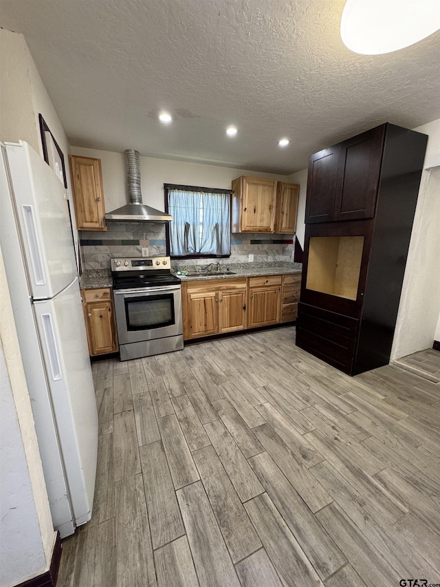 kitchen with wall chimney exhaust hood, stainless steel range with electric stovetop, freestanding refrigerator, and light wood-style floors