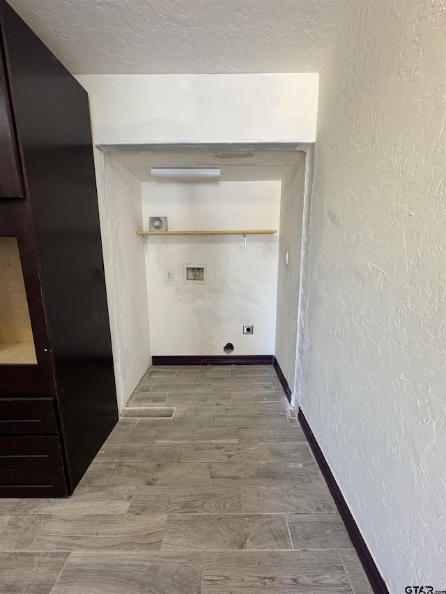 laundry area featuring wood finished floors, washer hookup, a textured wall, baseboards, and a textured ceiling