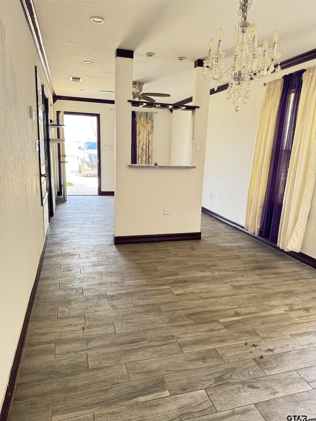 empty room featuring wood finished floors, crown molding, baseboards, and ceiling fan with notable chandelier