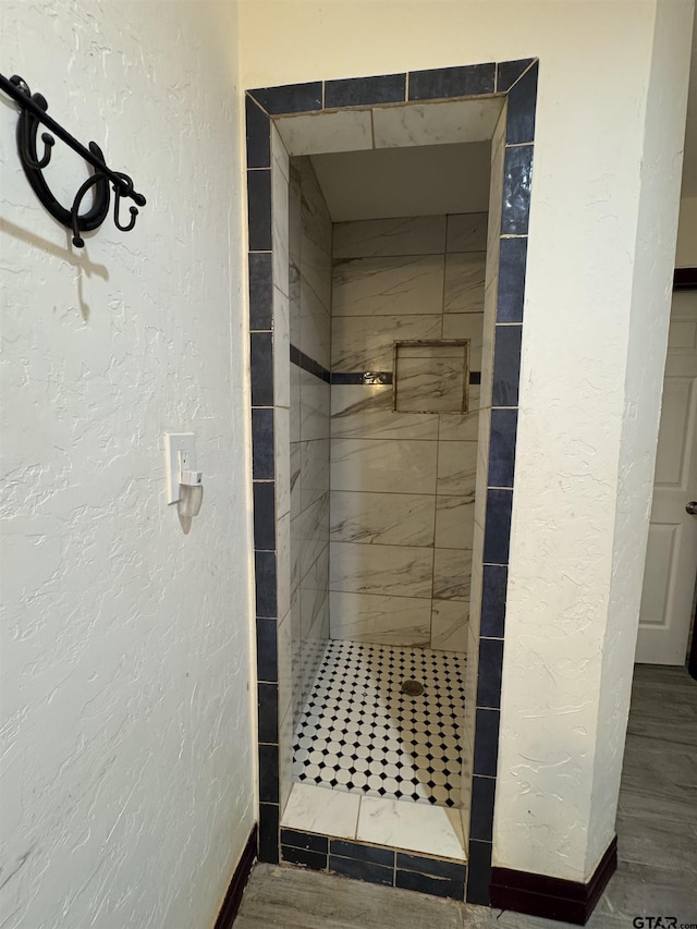 bathroom featuring a textured wall and a tile shower