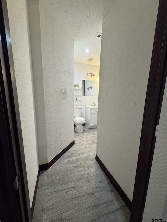hall featuring baseboards, wood finished floors, a textured ceiling, and a textured wall