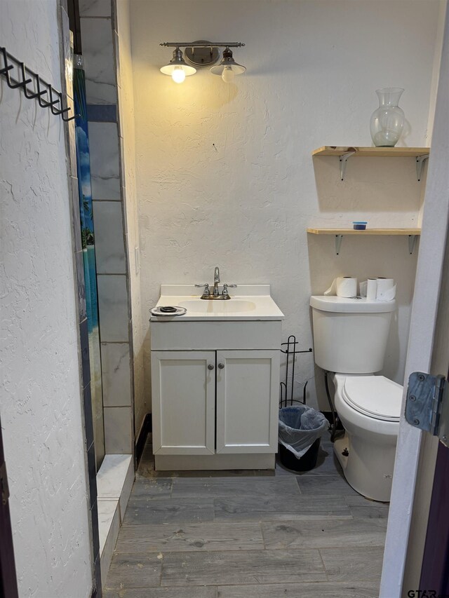 bathroom featuring toilet, vanity, a textured wall, and wood finished floors