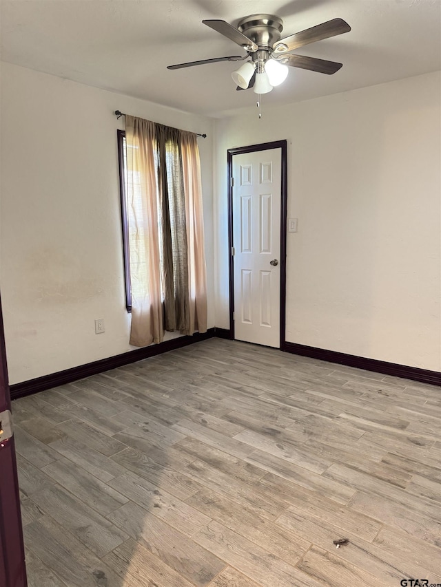 spare room featuring light wood-type flooring, a ceiling fan, and baseboards
