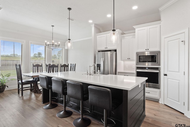 kitchen with a center island with sink, hanging light fixtures, stainless steel appliances, sink, and white cabinetry