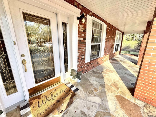 entrance to property featuring a porch and brick siding