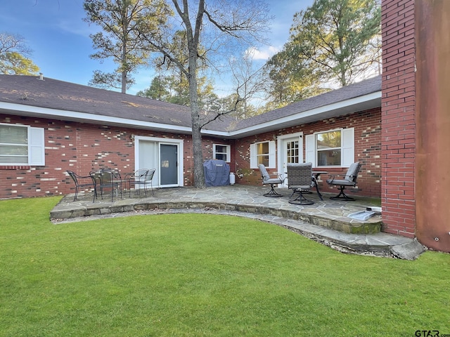 rear view of property featuring a yard, a patio area, brick siding, and a shingled roof