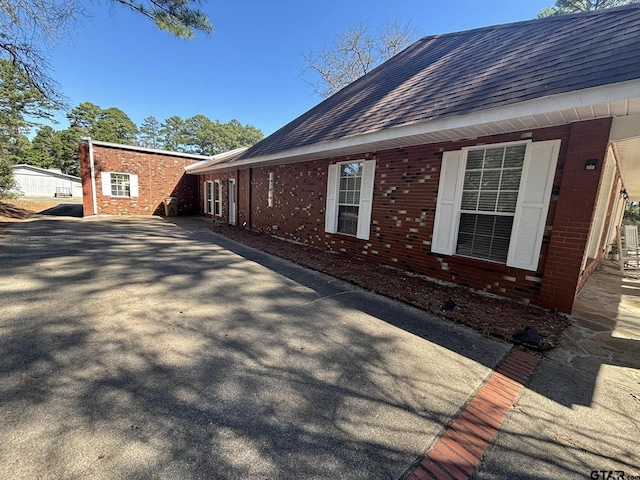 view of property exterior with a shingled roof and brick siding