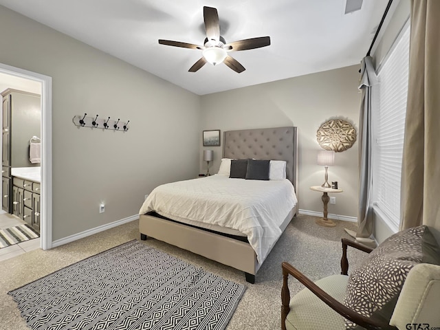 bedroom featuring baseboards, ensuite bathroom, a ceiling fan, and light colored carpet