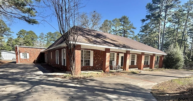 view of front of house featuring driveway, covered porch, and brick siding