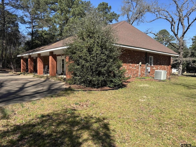 view of home's exterior featuring roof with shingles, brick siding, a lawn, and central AC unit