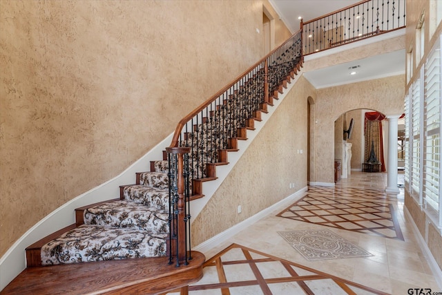 stairway featuring ornamental molding, a towering ceiling, and decorative columns