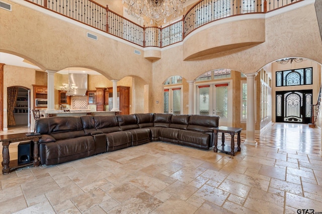 living room featuring a high ceiling, ornate columns, french doors, and a notable chandelier