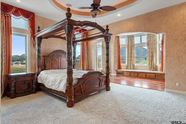 bedroom with hardwood / wood-style flooring, ceiling fan, and a raised ceiling