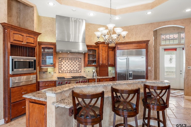 kitchen with built in appliances, ornamental molding, a kitchen island with sink, and wall chimney range hood