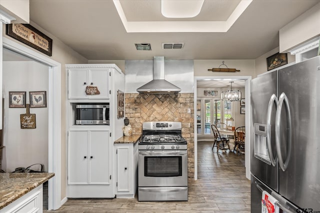 113 Granada Sq, Canton, TX 75103 - kitchen featuring appliances with stainless steel finishes, wall chimney exhaust hood, white cabinetry, a tray ceiling, and light stone countertops