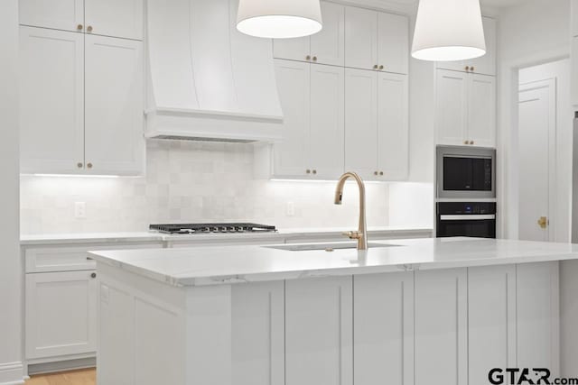 kitchen featuring light stone counters, decorative backsplash, custom range hood, appliances with stainless steel finishes, and white cabinetry