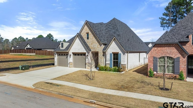 french country home featuring driveway, stone siding, fence, roof with shingles, and brick siding