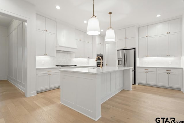 kitchen with light wood-type flooring, custom exhaust hood, stainless steel fridge, white cabinetry, and a sink