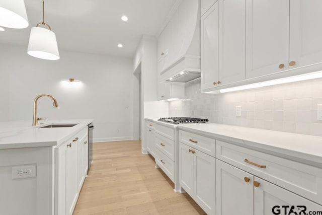 kitchen with light wood finished floors, backsplash, white cabinets, stainless steel appliances, and a sink