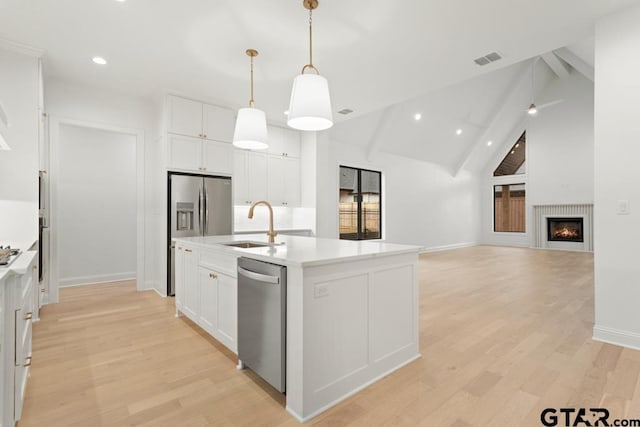 kitchen featuring an island with sink, a sink, appliances with stainless steel finishes, white cabinetry, and light wood-type flooring