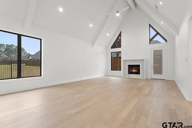 unfurnished living room featuring baseboards, high vaulted ceiling, beam ceiling, a lit fireplace, and light wood-type flooring