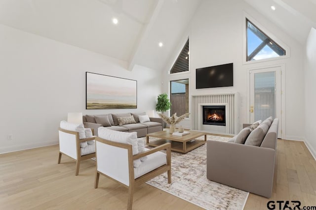 living room with light wood finished floors, baseboards, beamed ceiling, a lit fireplace, and high vaulted ceiling