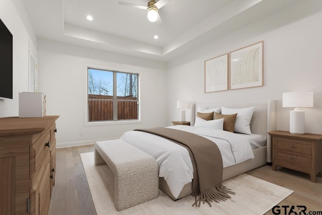 bedroom with recessed lighting, light wood-type flooring, and a tray ceiling