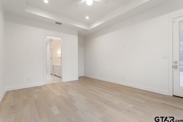 empty room featuring visible vents, baseboards, a tray ceiling, recessed lighting, and light wood-style floors