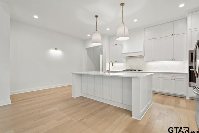 kitchen featuring backsplash, light countertops, custom range hood, light wood-style flooring, and a sink