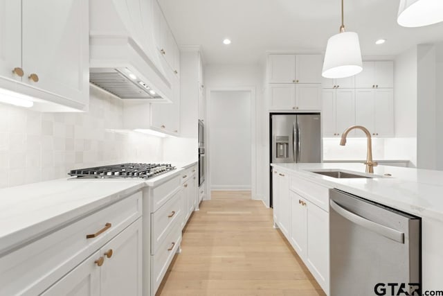 kitchen with premium range hood, light wood finished floors, a sink, white cabinets, and appliances with stainless steel finishes