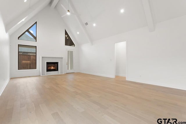 unfurnished living room with visible vents, high vaulted ceiling, beam ceiling, a lit fireplace, and light wood-type flooring