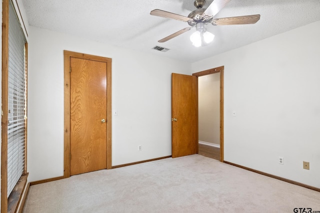 unfurnished bedroom featuring ceiling fan, light colored carpet, and a textured ceiling