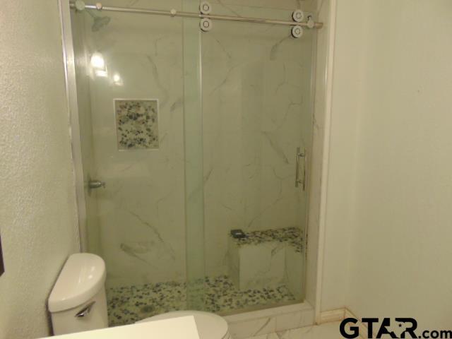 bathroom featuring a marble finish shower and toilet