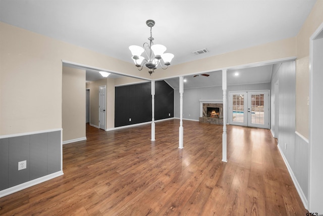 unfurnished dining area featuring wood-type flooring, an inviting chandelier, a fireplace, and french doors