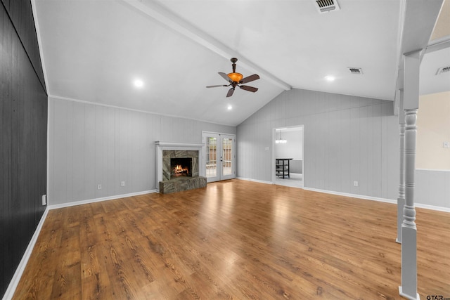 unfurnished living room featuring a stone fireplace, lofted ceiling with beams, ceiling fan, light hardwood / wood-style floors, and french doors