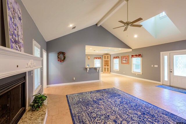 unfurnished living room featuring ceiling fan, beamed ceiling, a skylight, and high vaulted ceiling