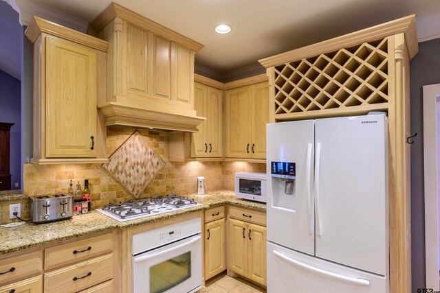 kitchen featuring tasteful backsplash, light stone counters, light brown cabinetry, and white appliances